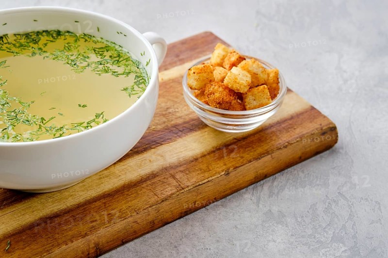 Closeup view of chicken stock with croutons on wooden serving board