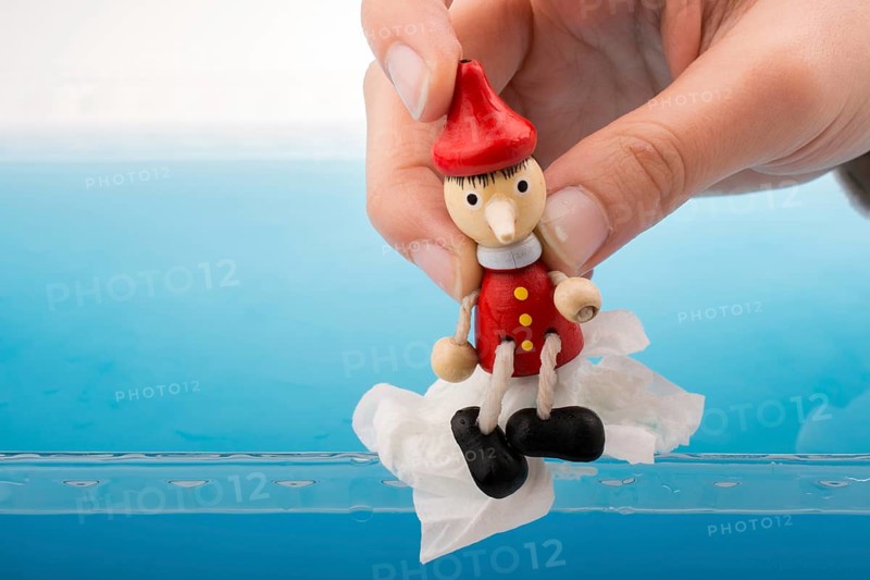 Hand holding wodden puppet Pinocchio on in blue water