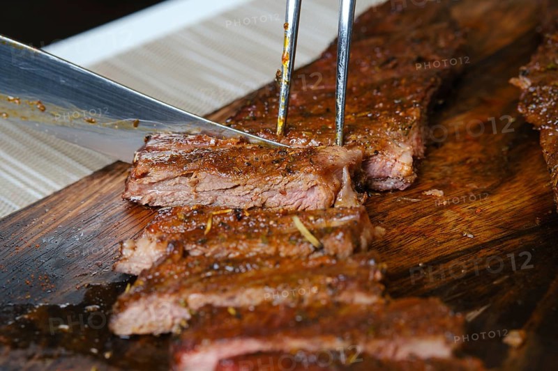 Cutting juicy grilled top blade beefsteak on wooden cutting board
