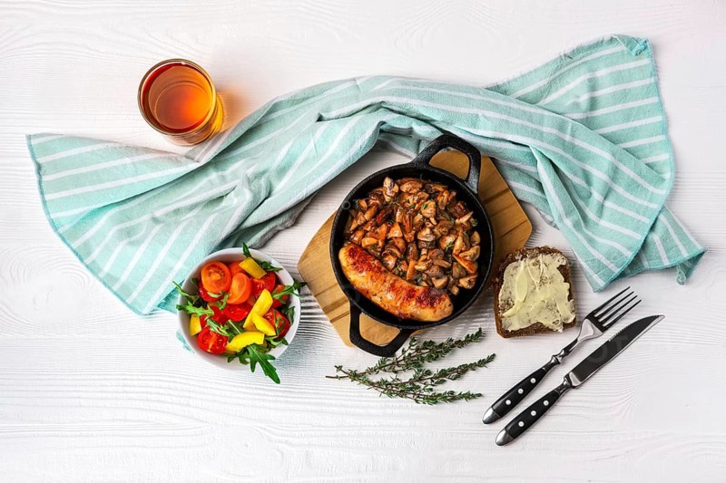 Cast-iron pan with fried sausage and mushrooms