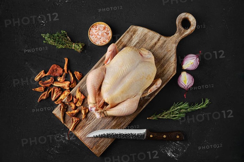 Raw whole broiler chicken with spices on wooden cutting board