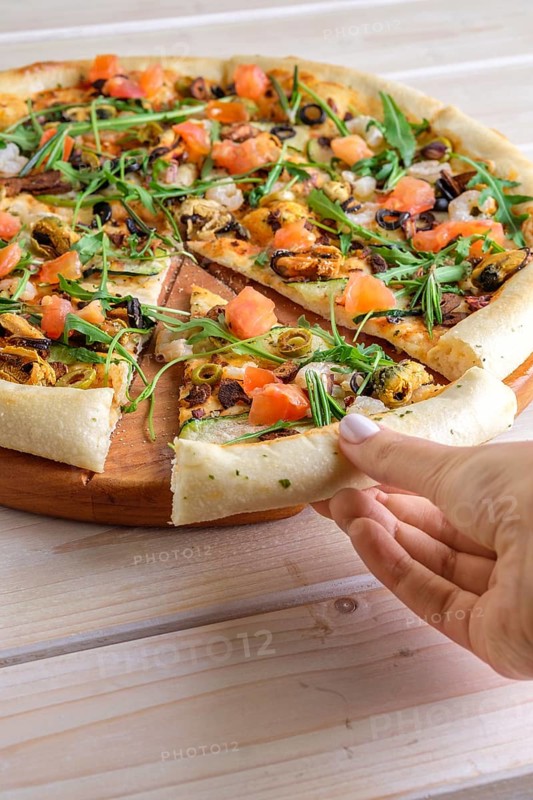 Hand picking slice of pizza with shrimps