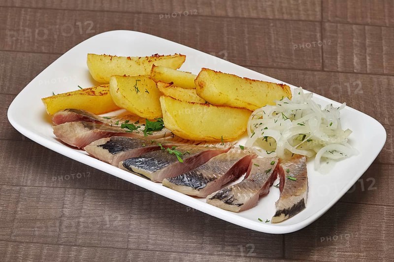 Plate with pickled herring and onion with potato wedges on wooden table