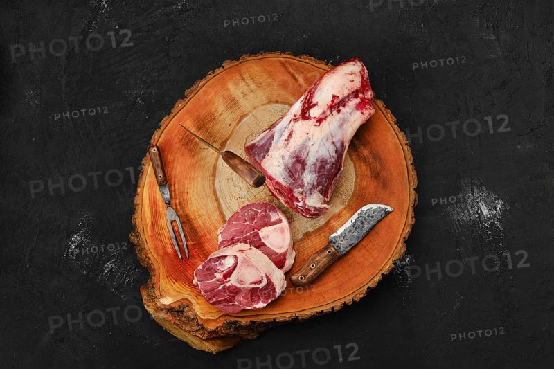 Chopping ossobuco steak from beef shank with cleaver on wooden stump