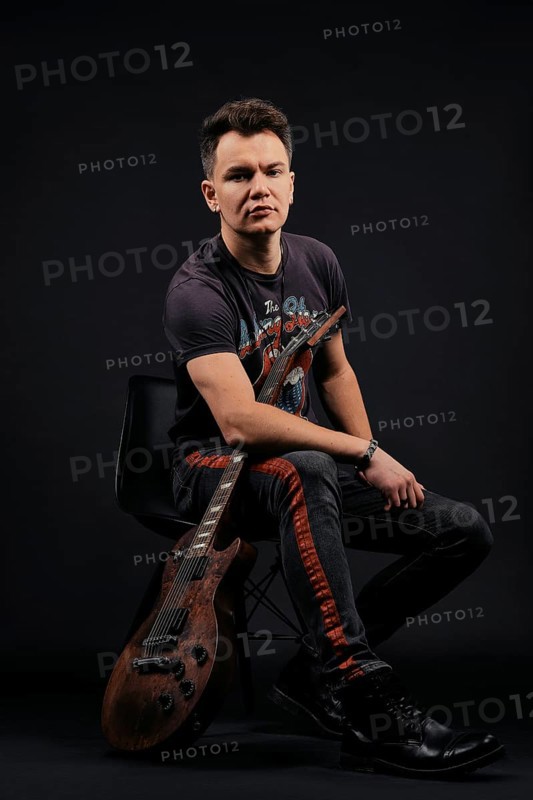 Low key portrait of musician sitting on chair with electro guitar