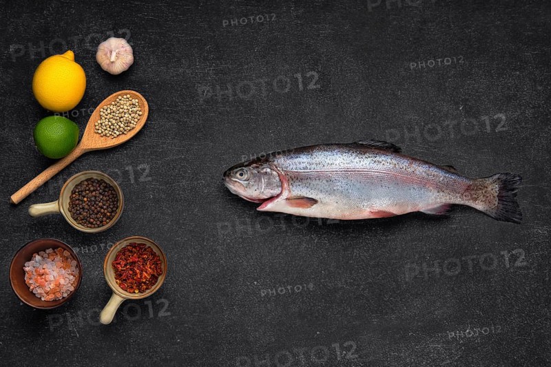 Overhead view of fresh raw trout with spice on black stone background