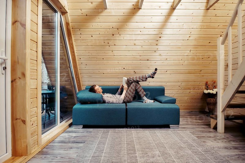 Middle aged man relaxing with book on sofa at chalet. Man in checkered trousers