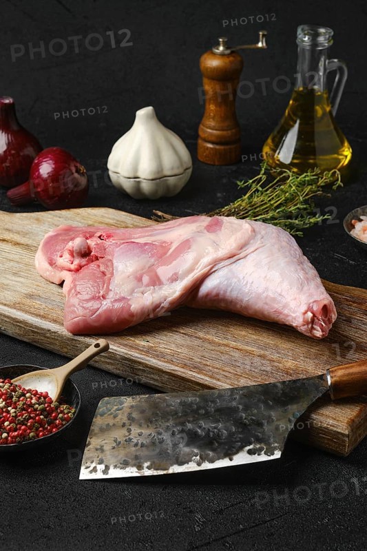 Raw turkey leg with skin on cutting board with cooking ingredients on black background