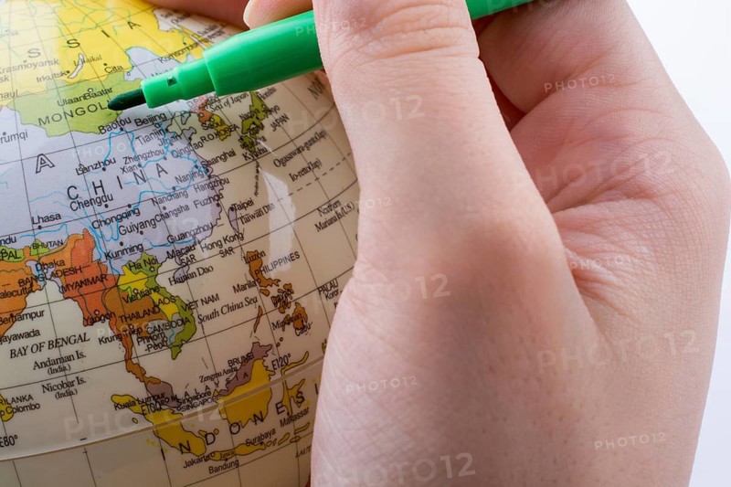 Hand holding a grren color pen on a little model globe on white