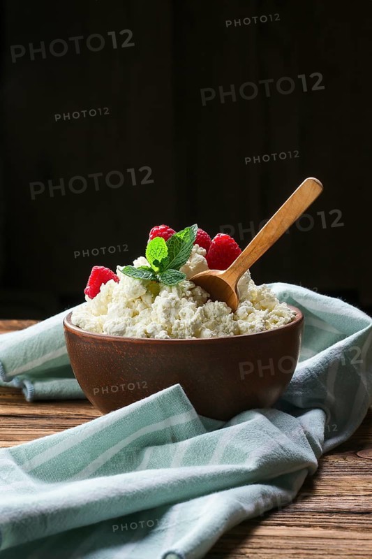 Fresh cottage cheese with raspberries and wooden spoon in clayware on wooden table