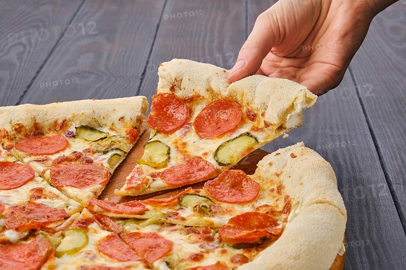 Hand taking slice of pizza pepperoni from plate