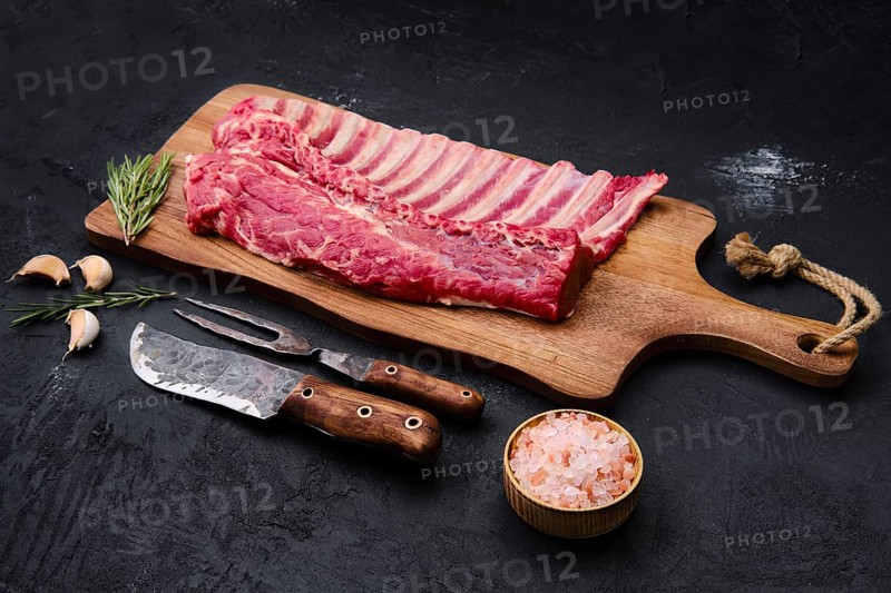 Fresh raw rack of lamb on wooden cutting board with herbs and seasoning