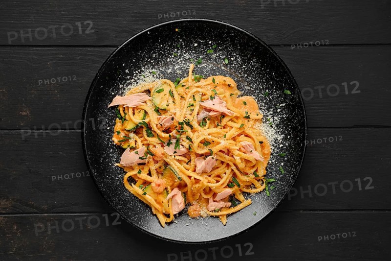 Top view of pasta with salmon and zuccini with grated parmesan on a plate