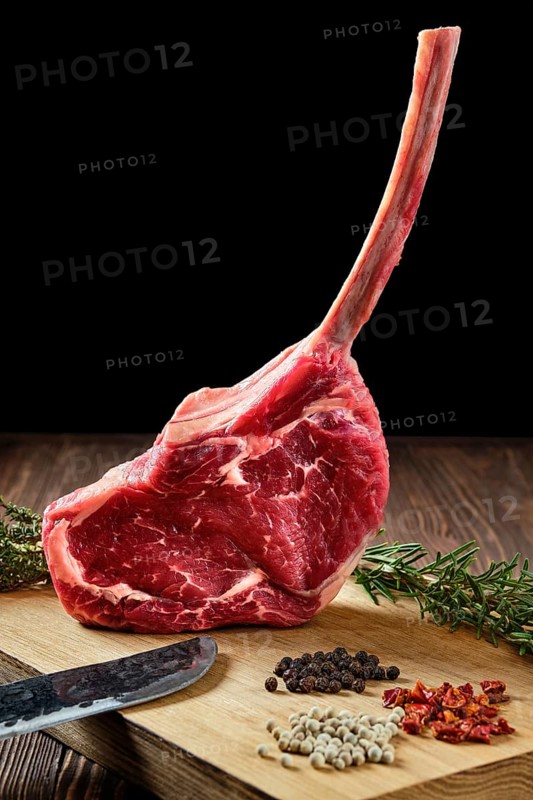 Close up of raw cowboy steak on wooden cutting board with spice