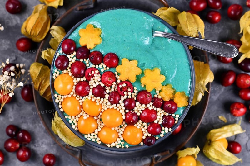 Fruit smoothie bowl with healthy natural green spirulina powder decorated with cranberries