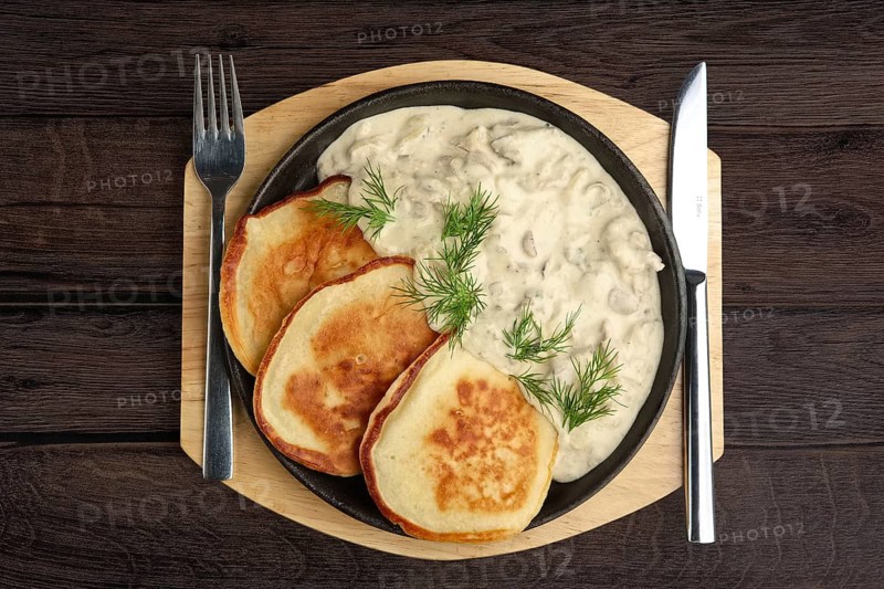 Flapjack with mushroom sauce on wooden plate. Top view