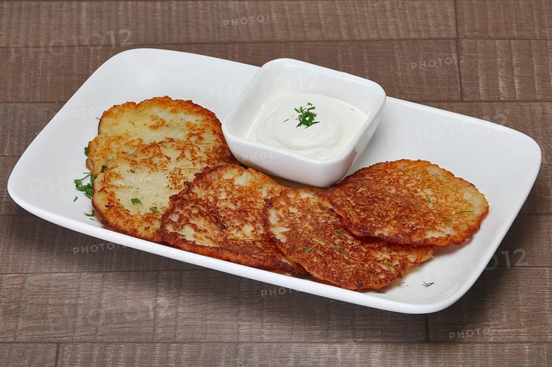 Traditional belorussian potato pancakes with machanka sauce on wooden table