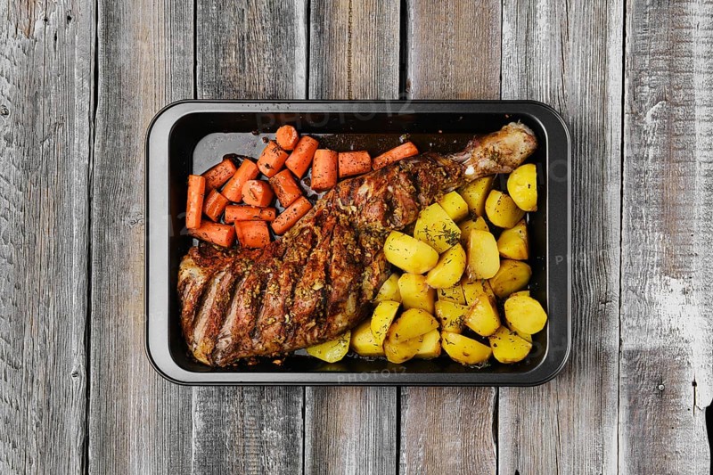 Overhead view of baked in oven lamb shoulder with potato and carrot in oven-tray