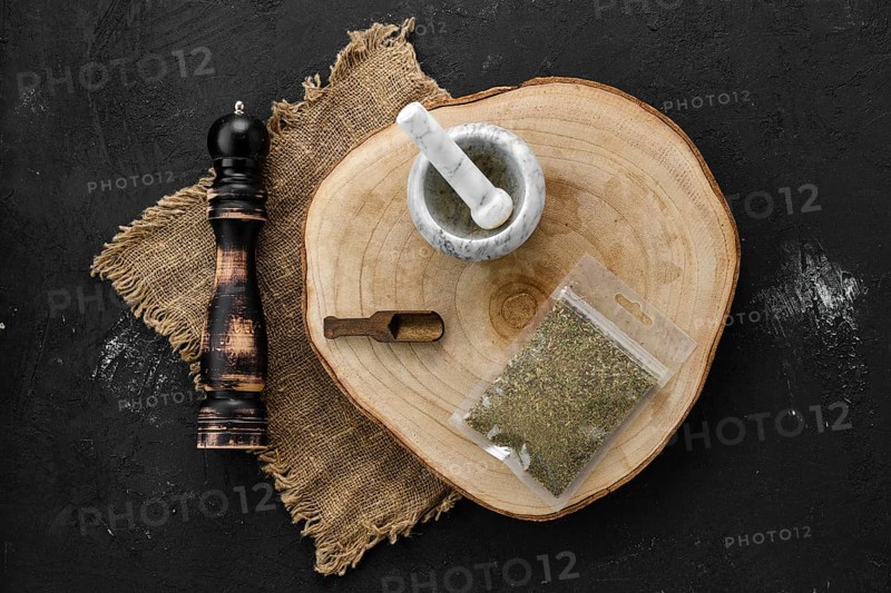 Wooden cross section with Provencal herbs in plastic package and stone mortar and mill