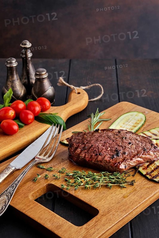 Beef steak and zucchini served with fresh tomato cherry and basil on wooden cutting board