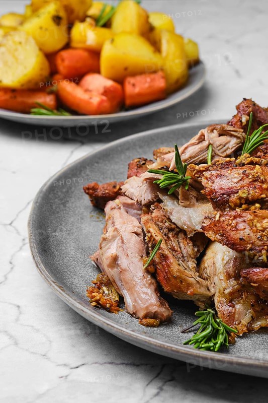 Closeup view of pulled lamb shoulder meat baked in oven with potato and carrot on marble table