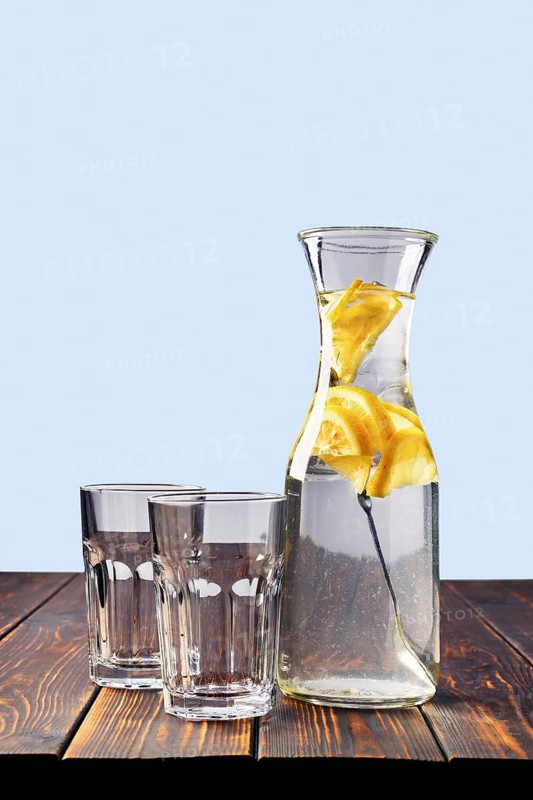 Jug with cold water with ice and lemon and two empty glass on the table with space for inscription