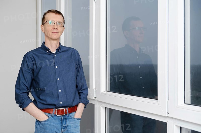 Middle-aged man is standing with hands in pockets on balcony in the early morning