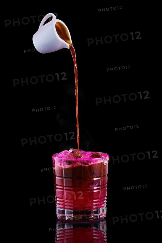 Pouring hot espresso in glass with tonic and dragon fruit syrup isolated on black background