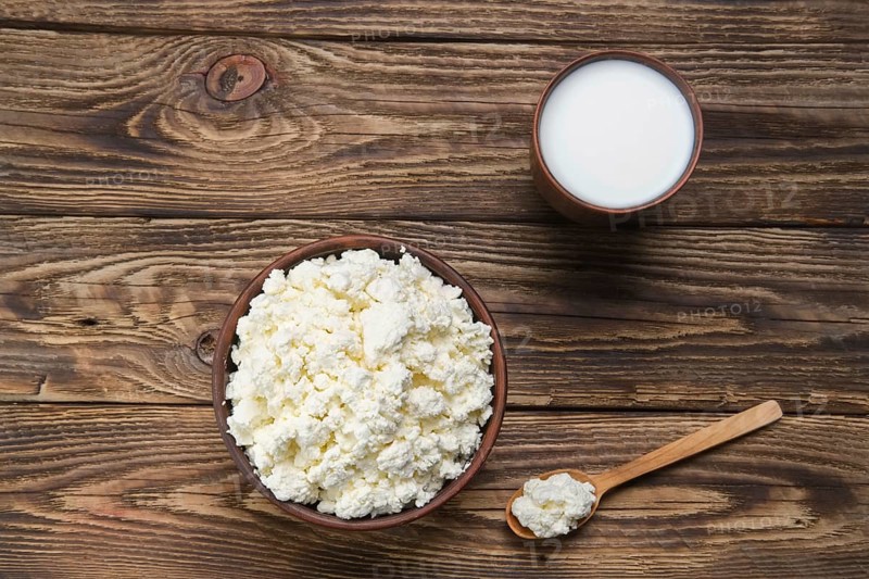 Fresh cottage cheese in clay bowl with wooden spoon with a glass of milk on rustic wooden background