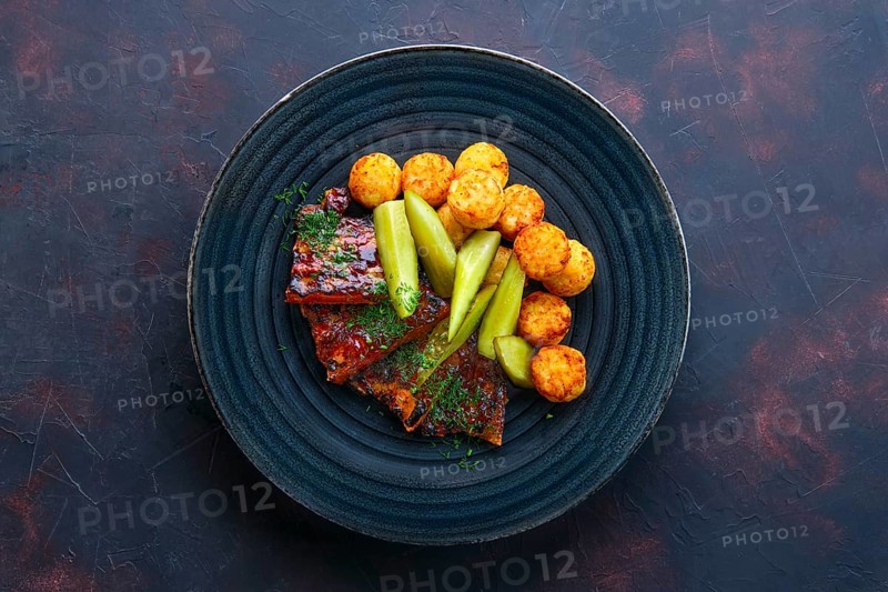 Top view of grilled ribs with pickled cucumber and fried potato balls