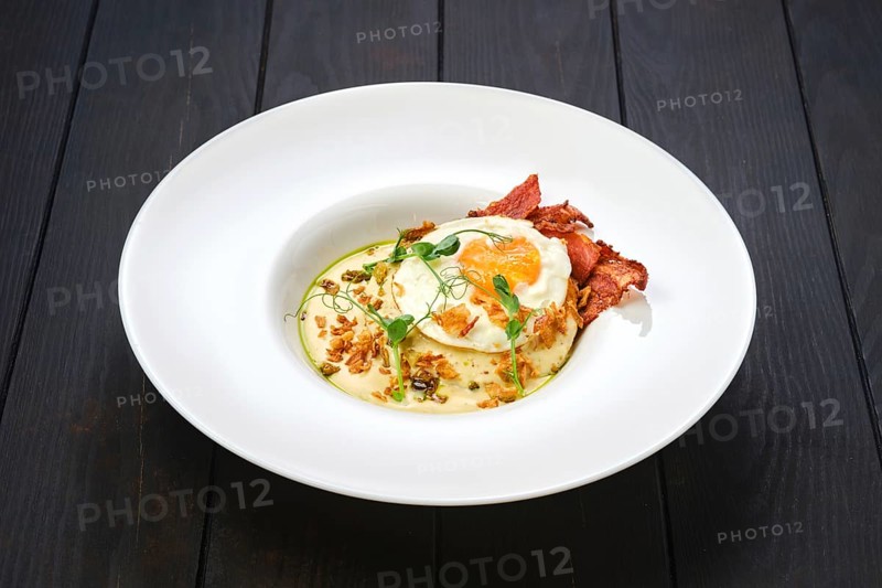 Fried egg with bacon slices and chips served with creamy sauce
