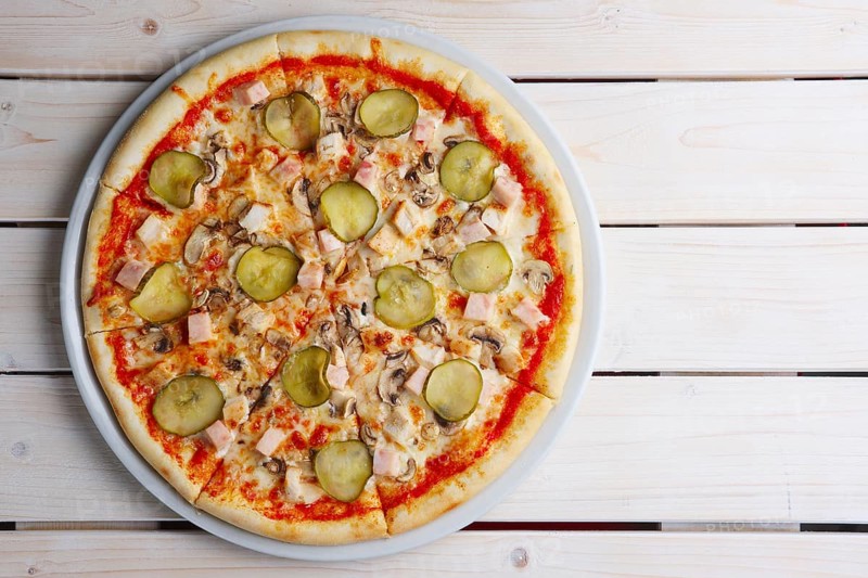 Top view of pizza with ham and pickled cucumber