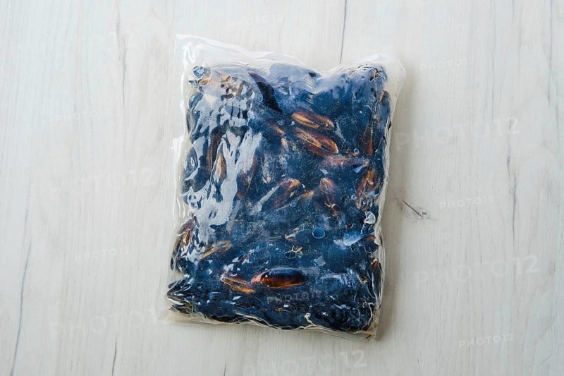 Cooked frozen mussels meat in vacuum packaging on wooden table