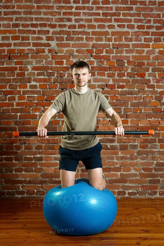 Athletic man doing exercises for the balance on rubber ball with gymnastic stick. Fitness workout