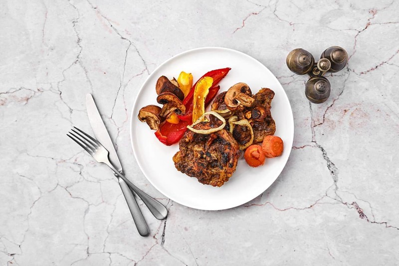 Overhead view of lamb neck with champignon and vegetables baked in oven on a plate