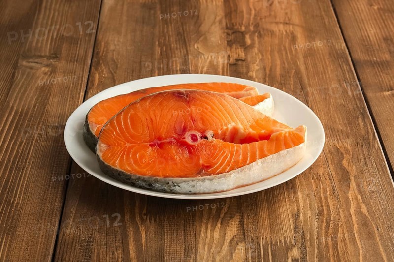 Two pieces of fresh salmom steak on a plate on wooden table