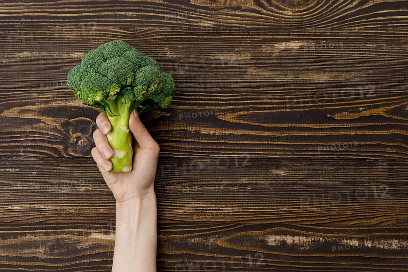Overhead view of fresh broccoli in hands over wooden background