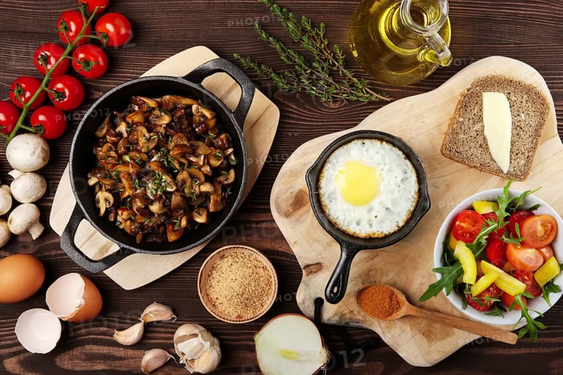 Vegetarian food. Fried mushrooms and egg in cast iron pan. Ingredients for rustic breakfast on wooden table