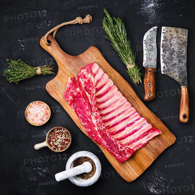 Fresh raw rack of lamb on wooden cutting board with herbs and seasoning