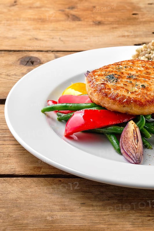 Close up view of salmon cutlet with roasted vegetables and green buckwheat