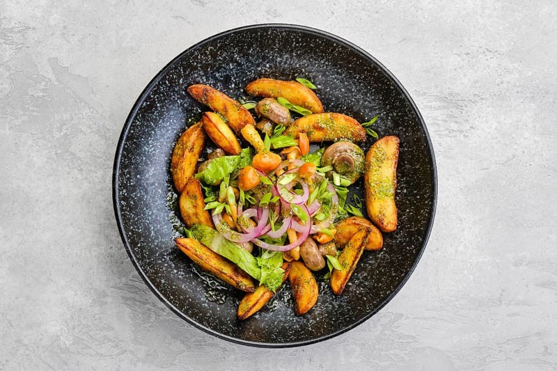 Top view of fried potato wedges with champignons dressed with red and white onion