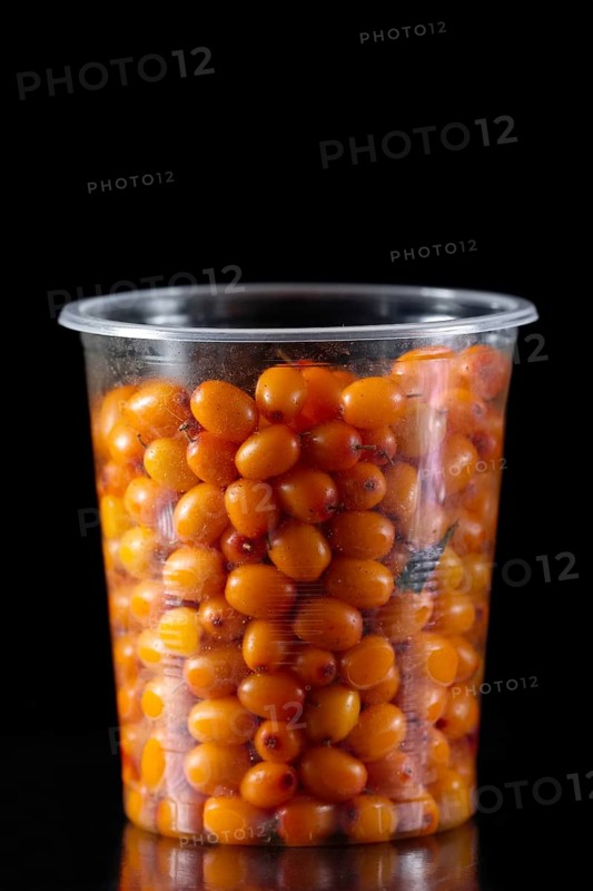 Plastic glass full of sea buckthorn on black background