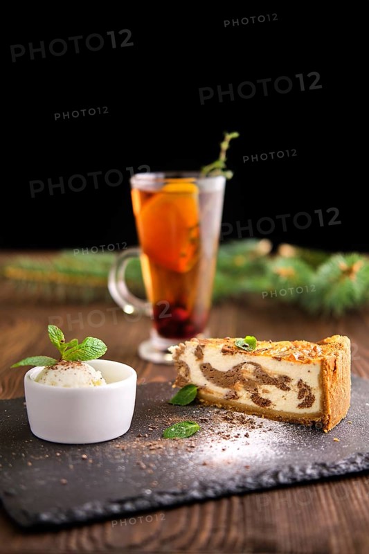 Layered cheesecake with ice cream and fruit tea served on slate plate on dark wooden background