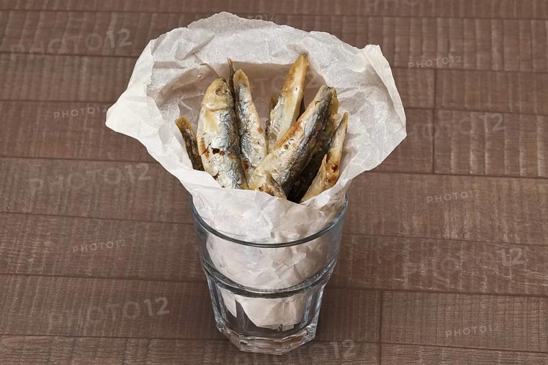 Fried sprat in rough facetted glass in wrapping paper on wooden table