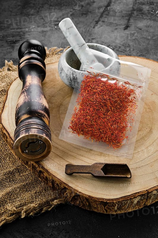 Wooden cross section with saffron in plastic package and stone mortar and mill
