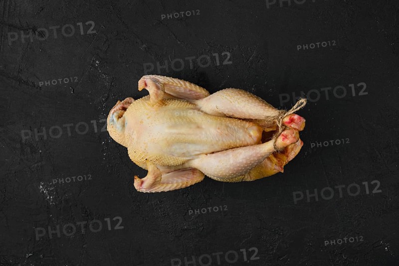 Raw whole chicken with spices on wooden cutting board