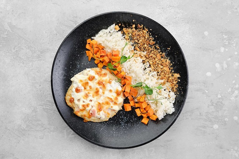 Chopped pork cutlet baked with ham and cheese served with carrot and rice on a plate