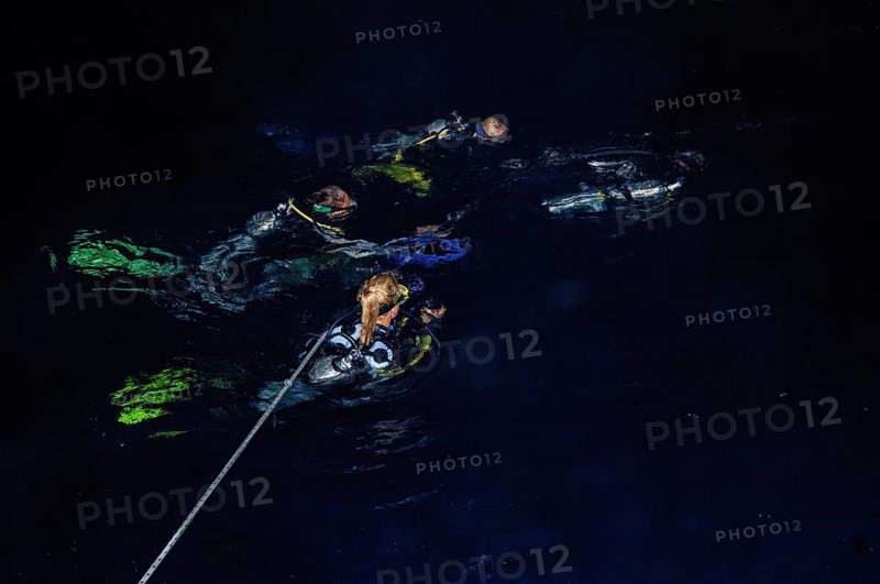 Divers swim at night on boat line line from dive boat sea surface water surface prepare for descent for night dive