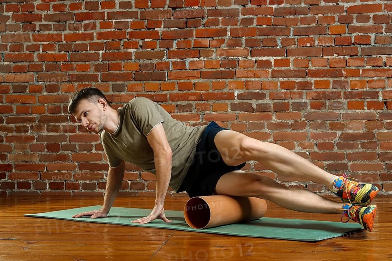 Young male cyclist athlete training and doing workout with barrel on gym mat. Fitness workout