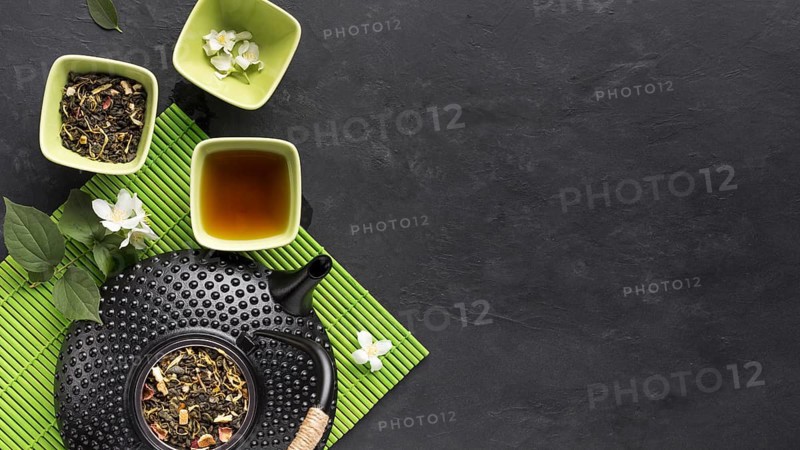 Raw herbal tea ingredient with teapot green placemat black surface